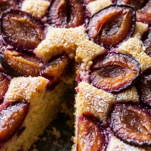 Angeschnittener Zwetschgenkuchen mit Puderzucker bestäubt, serviert auf einem Holztisch